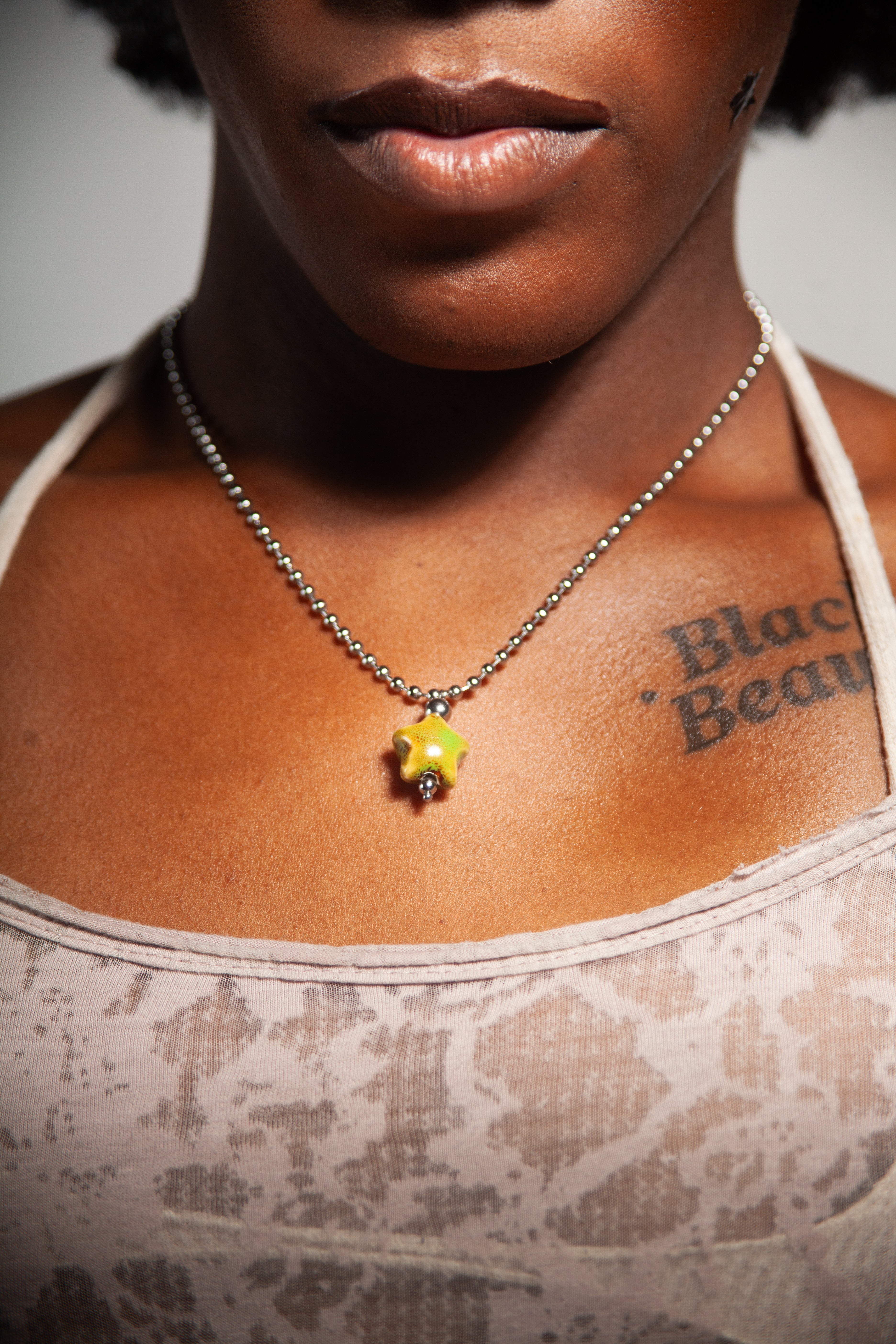 Person wearing a necklace with a green pendant, visible tattoo on chest.